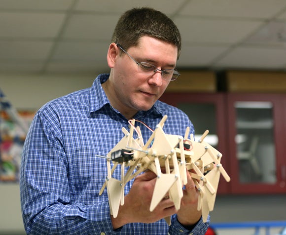 Instructor Kevin Dietsche examines a mechanical-electrical “scrawler,” a 12-legged walking device created by Matthew Harris.