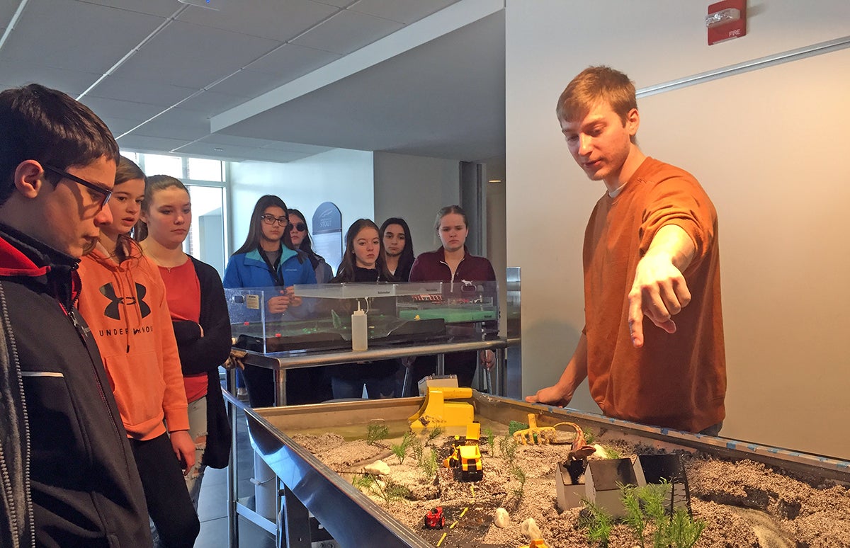 UW-Stout student Evan Harding explains a stream table model to middle school students at Stout Connects You Thursday, Feb. 27.