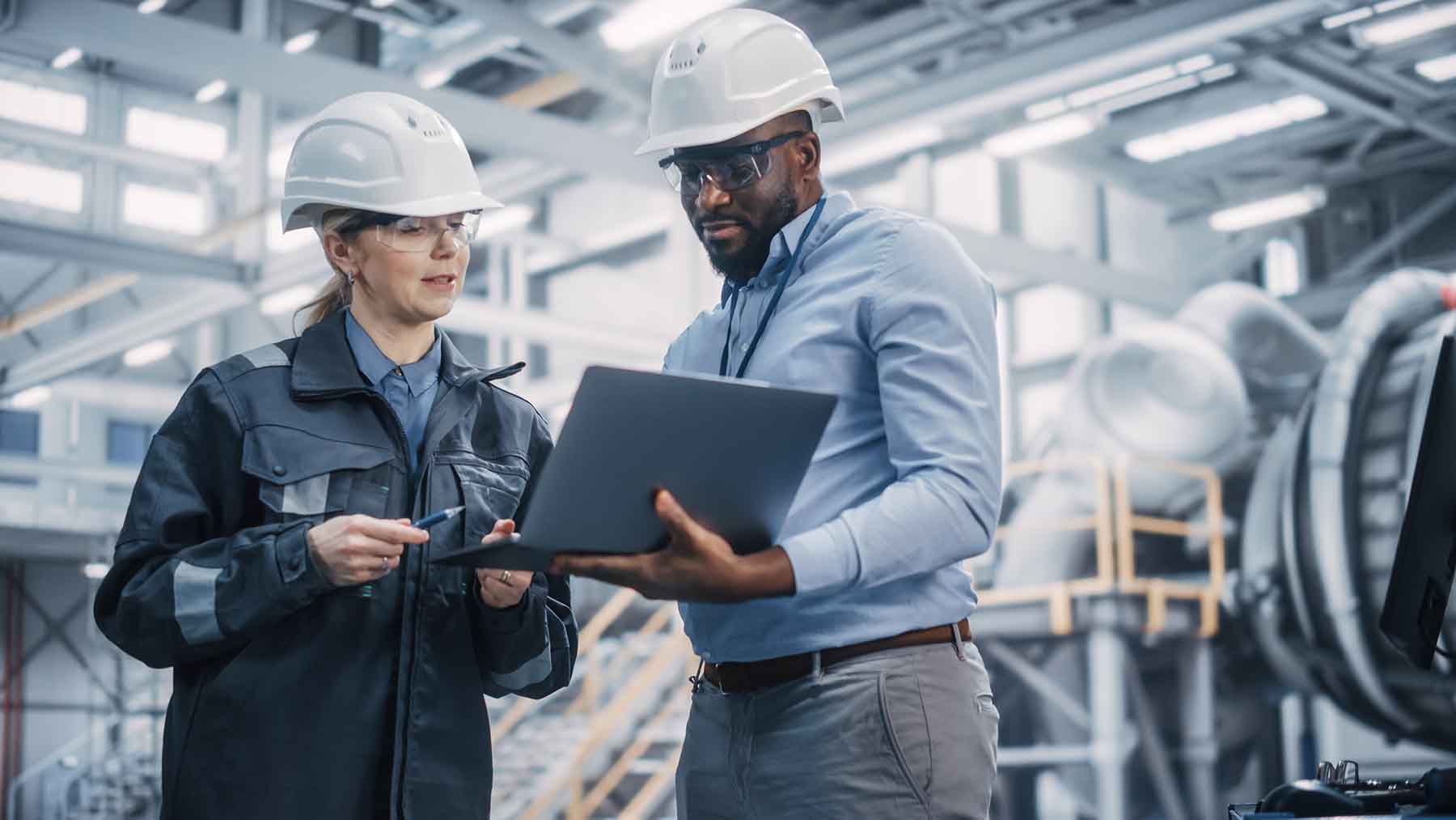 Two individuals in hardhats employee performance in a manufacturing center.