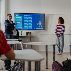 An instructor and student stand near a screen showing a Mathematics and AI Learning lesson in a modern classroom.