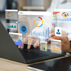 Hands typing on a laptop with holographic data dashboards showing charts, graphs, and analytics floating above the screen