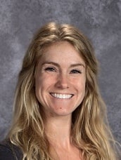 Cheyenne Braker is a white woman with wavy blonde hair. She is smiling at the camera in front of a gray background.