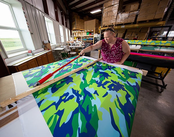 Deb Techmeier cuts custom fabric to make a designer laundry bag for a summer camper. She sewed the bag at another production station.