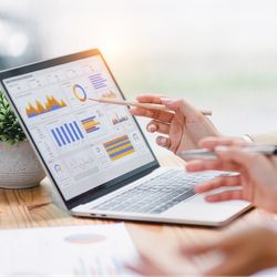 Close-up of a person using a pencil to point at colorful performance charts and analytics graphs on a laptop screen.