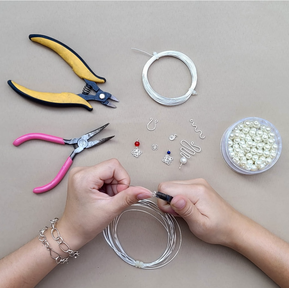 An image of hands creating earrings using wire and tools