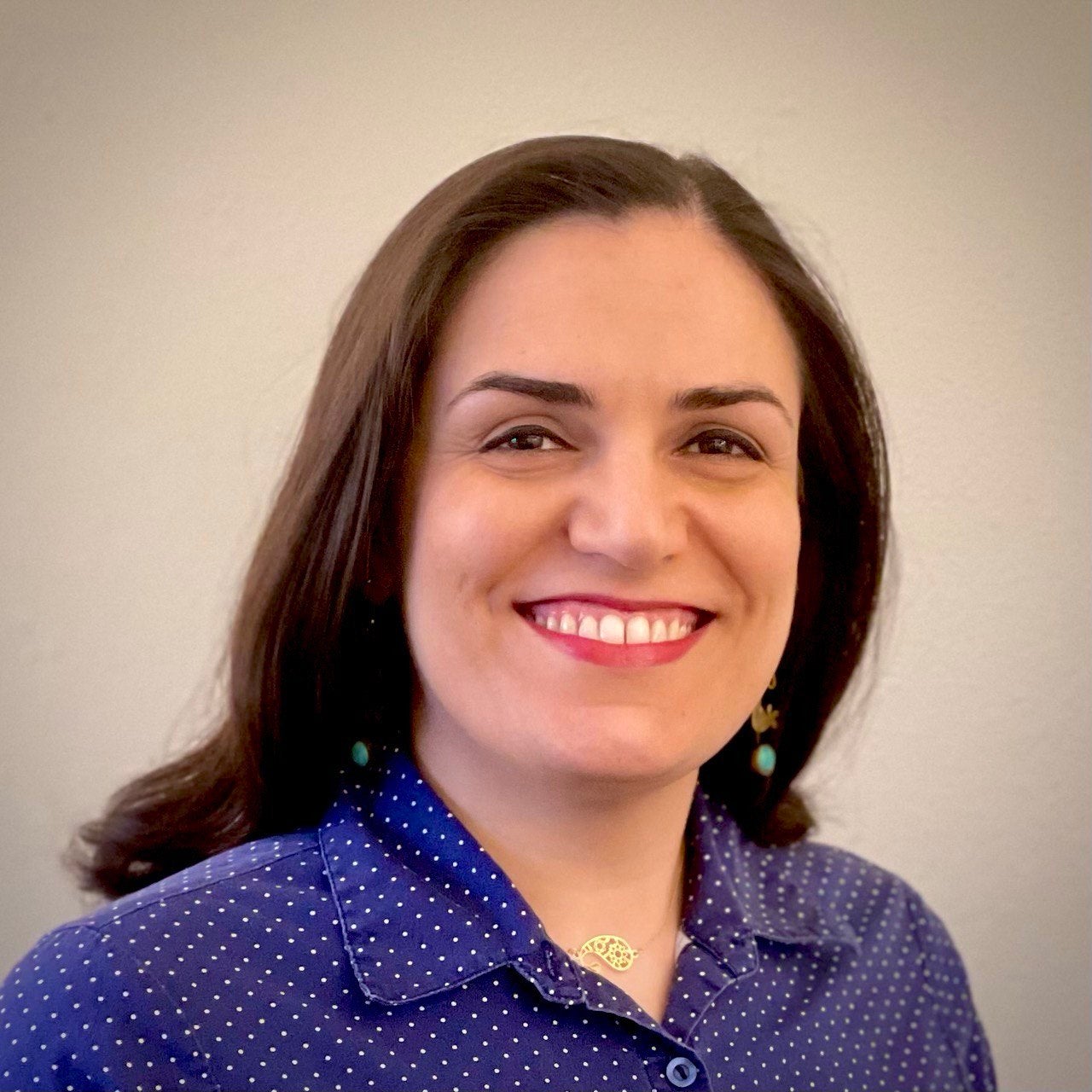 Ellie Nikoo, a woman with brown hair and brown eyes, is smiling at the camera. She is wearing a blue shirt.