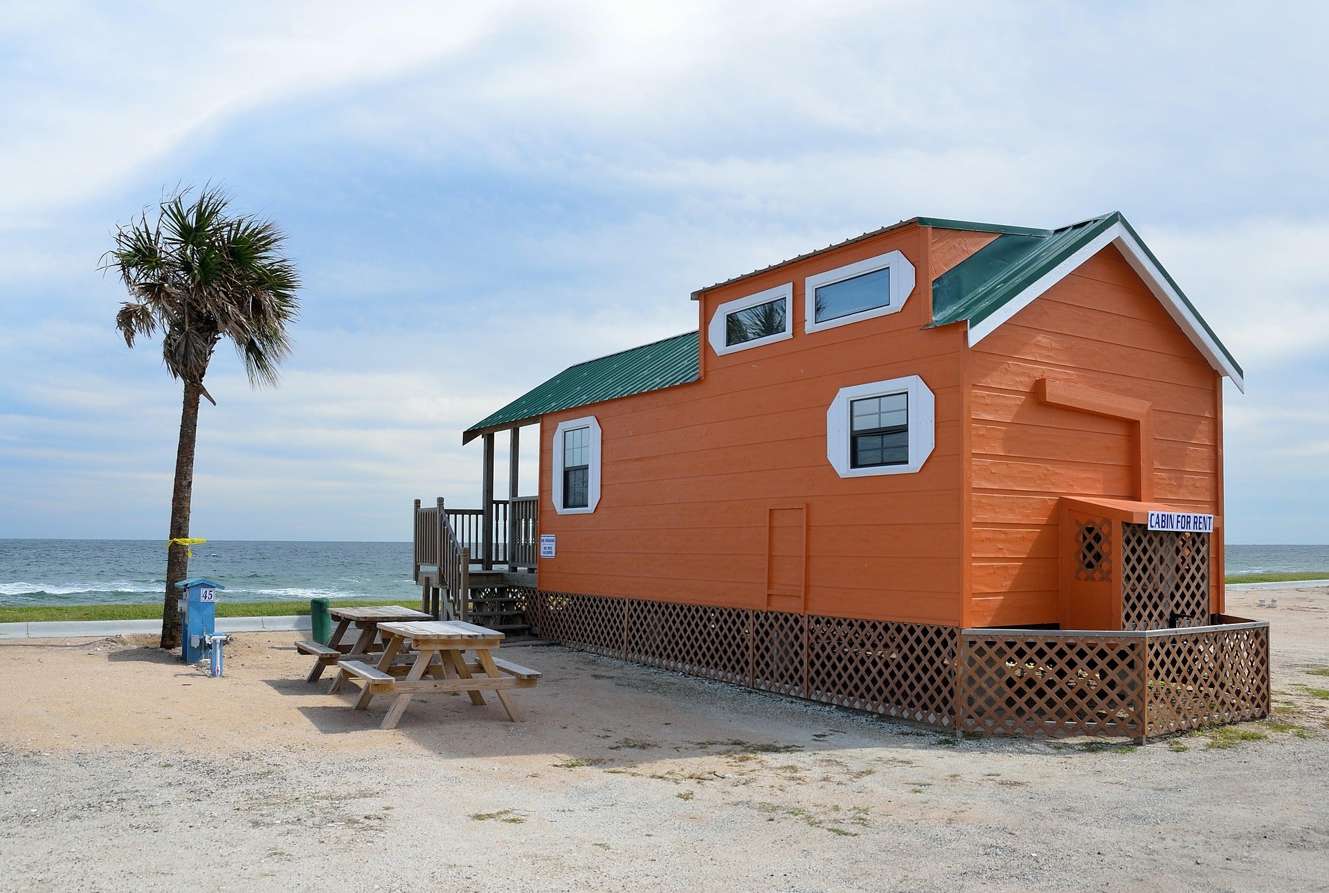 Small cottage on a beach with a palm tree and picnic tables