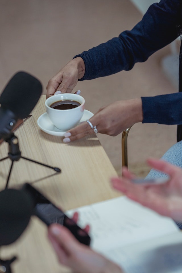 person setting a coffee cup down near a laptop with a mic in the background