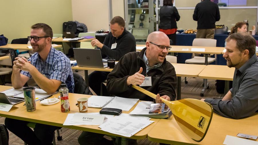 Ed Vater from Branches, LLC, foreground center, discusses business with Jeff Carr, Senior Project Manager from the UW-Stout Manufacturing Outreach Center, as he shows Jeff the BB Special canoe paddle.
