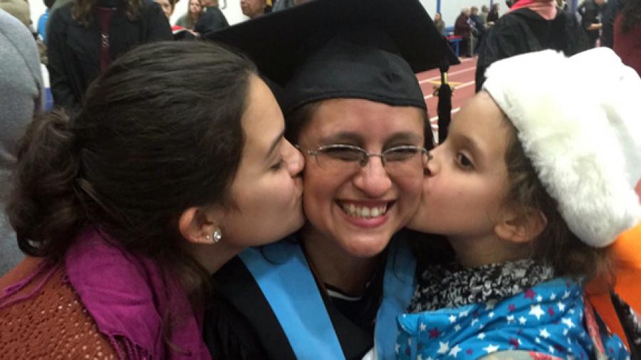 Online student Veronica Solano receives a congratulatory kiss after commencement from daughters, Nasim, left, and Anisa.