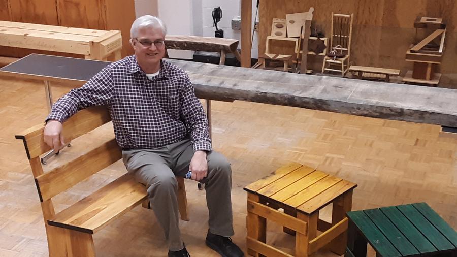 UW-Stout Professor Jerome “Jerry” Johnson sits on one of the benches made by students he has worked with since 2017, as part of a Menomonie Urban Forestry Board project.