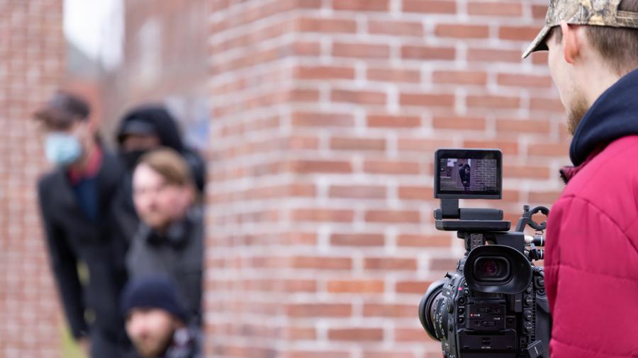 A student films other students as they try a camera on a tripod outside during the workshop.