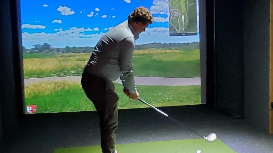 A student takes a shot during a Kohler Hospitality overnight trip at a golf simulator in the Kohler Swing Studio and Golf Shop.