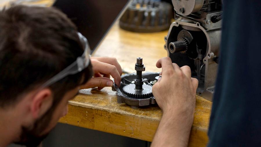 A close-up photo of students hands working on a small engine