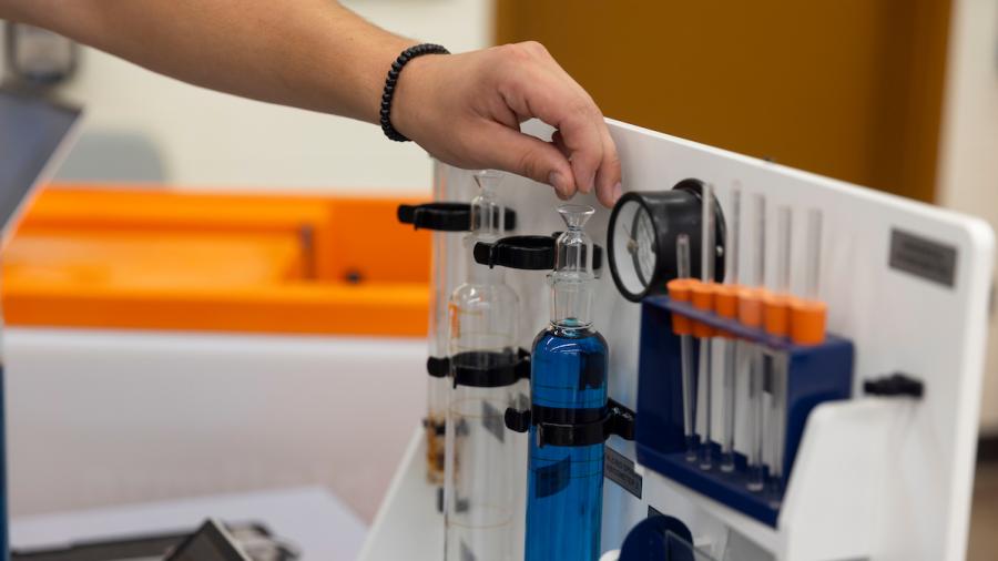 A student dropping ball bearings into a vial of blue liquid