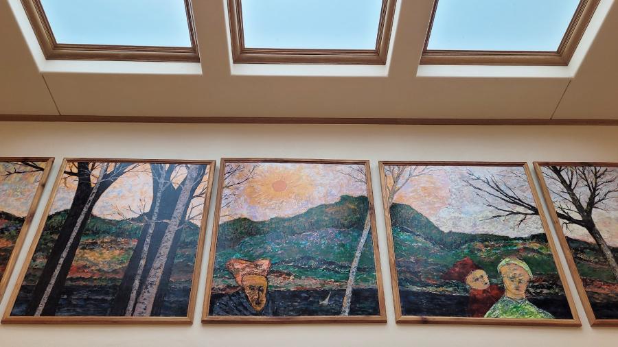 Paintings of hills, trees and people under a skylight.