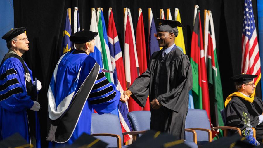 A graduate crosses the commencement stage to receive his diploma and congratulations from Chancellor Frank.