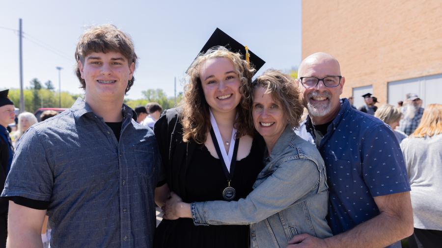 A student celebrates at commencement with family on a sunny day.