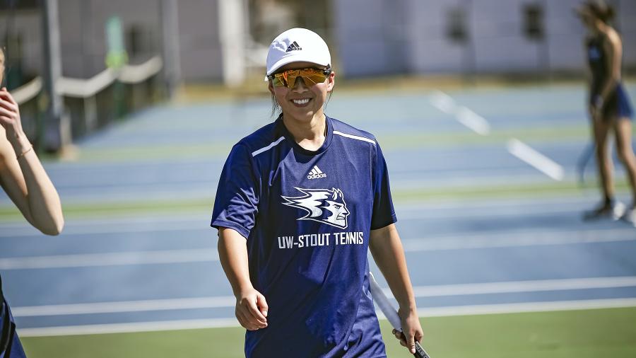 A student athlete smiles on the tennis court.