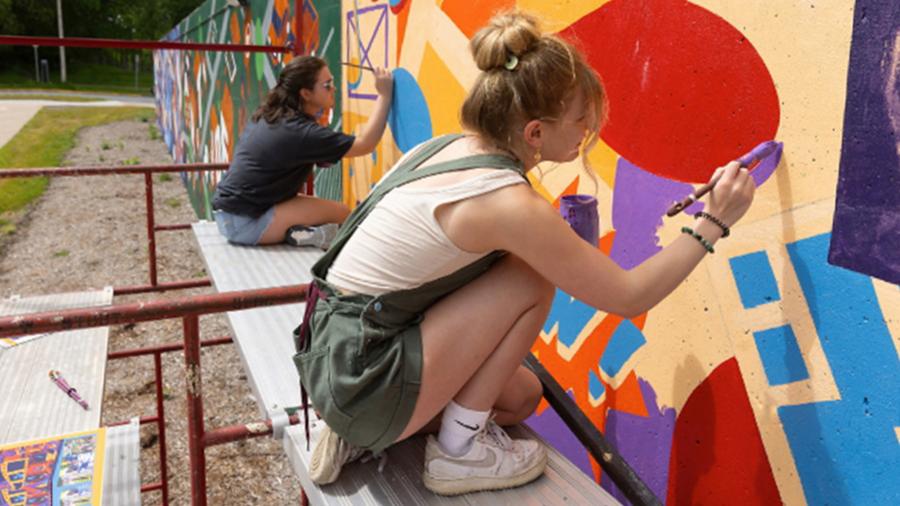 A student helps to paint a mural on a loading dock wall