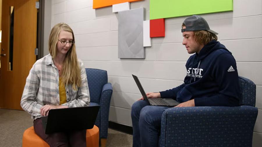 Two students study on their laptops in a study lounge