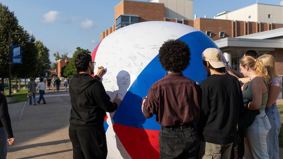 Students sign an enormous beach ball at at involvement fair