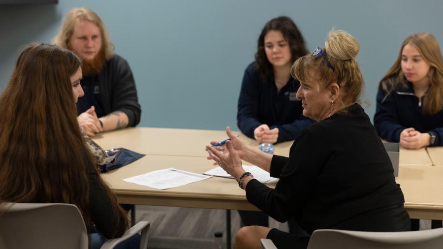 A teacher talks with four students as they sit around a table