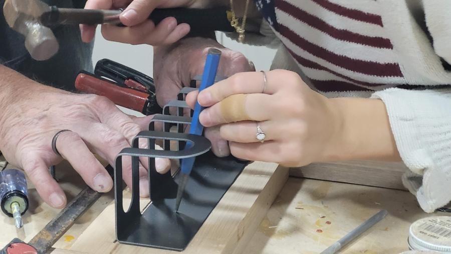An industrial design student hammers countersinks into a metal plate.