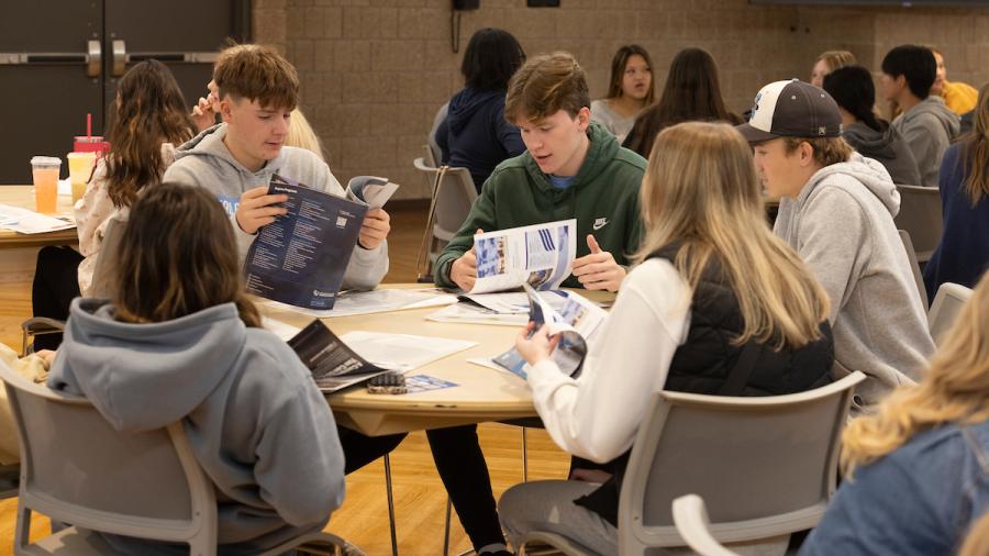 Students sit at a round table and look through education program brochures.