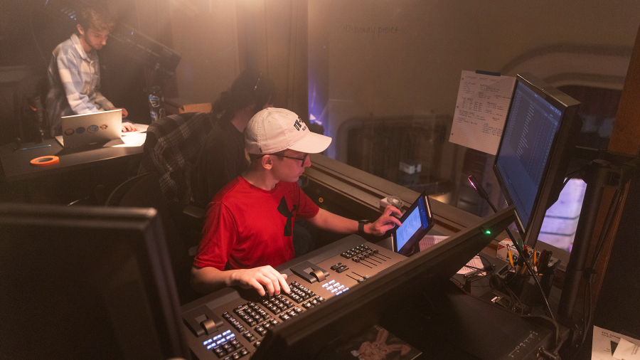 A Stout student mixes lighting and sound for a theatre production, while her colleagues attend to other production consideration
