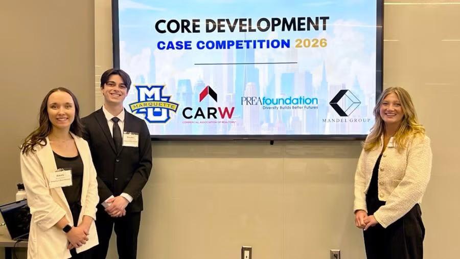 Three people in business attire stand in front of a large screen displaying “Core Development Case Competition 2026” with Marquette University and partner logos.
