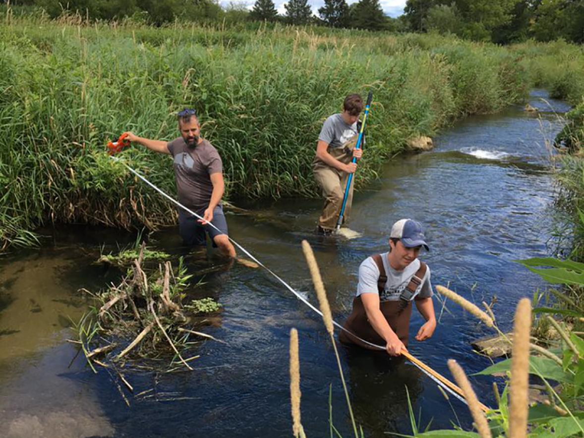 Keith Gilland, left, Kal Breeden, foreground and Dylan Kostuch measure stream width this summer as part of their research.