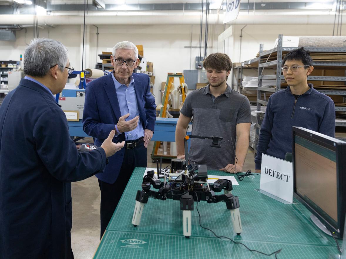 UW-Stout Assistant Professor Yuan Xing, right, meets with Gov. Tony Evers, second from left, to demonstrate the AI-based robotic system he is developing to help determine the freshness of fruit in warehouses.