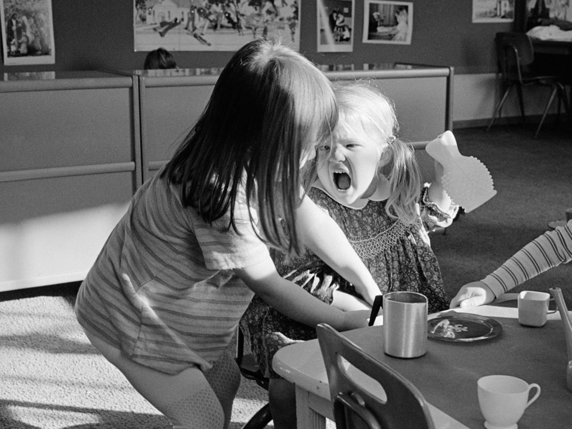 Two small children lean into each other and one cries in a black and white photo.