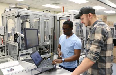 Mechanical engineering students Kefa Okoth (left) and Ben Miner look at their prototype designs of a product they plan to produce with manufacturing equipment.