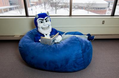 UW-Stout's mascot Blaze the Blue Devil reading in the library.