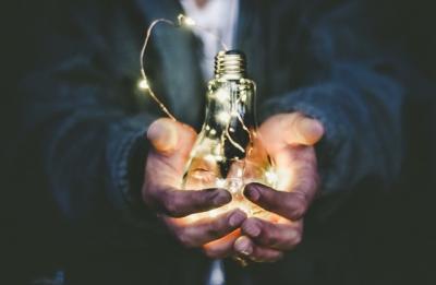 Two hands holding a glowing light bulb.