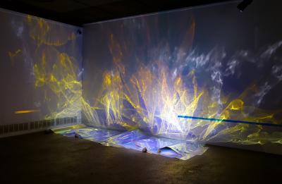 Sheets of reflective, colorful paper are layed on the floor and illuminated, causing the walls to glow with an aurora borealis of colors