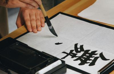 Person using Japanese brush, ink and paper to create calligraphy