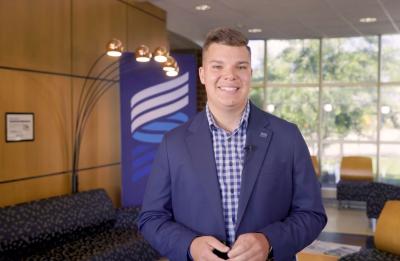 Student stands indoors in a campus lounge area with UW-Stout branding visible behind.