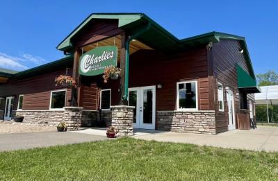 Exterior view of a rustic-style building with stone accents and a sign reading “Charles Bar & Grill at Northwood Hills,” with outdoor seating nearby.