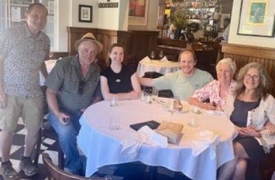 Six people seated and standing around a dining table inside a restaurant.