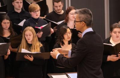 A choir in formal attire performing, conducted by Dr. Jerry Hui standing in front