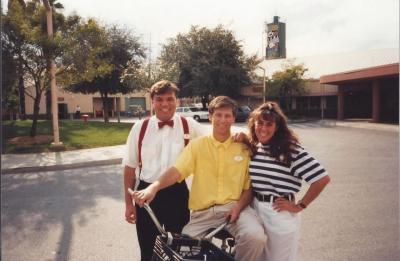 Three Disney cast members pose outdoors near a bicycle during the early years of their careers.
