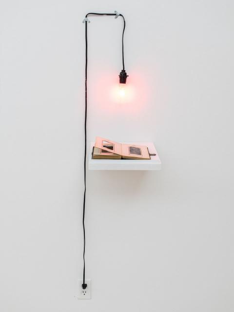 A red light bulb burns above a tome. By Beck Slack.