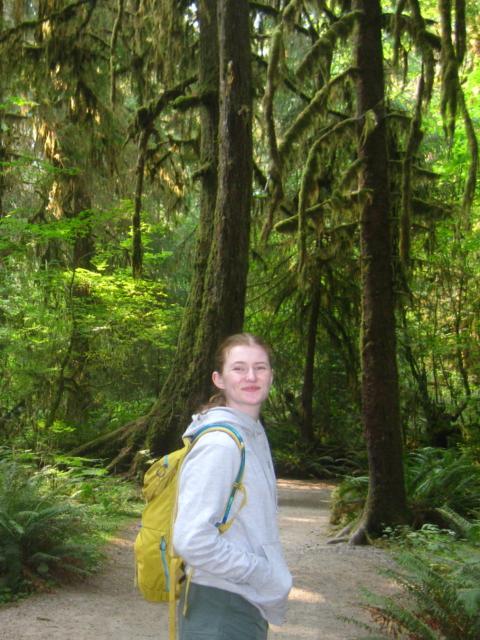 A student poses on a trail on hike in the woods.