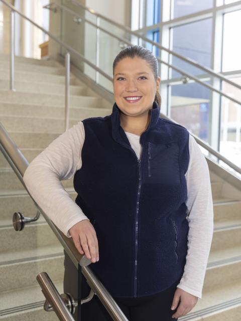 UW‑Stout student ambassador poses on an indoor staircase inside a campus building.