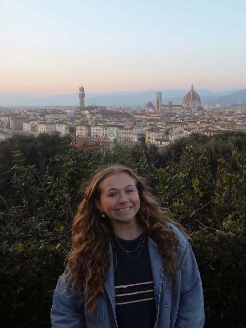 Person smiling with Florence skyline at dusk, framed by greenery with the Duomo and bell tower in the distance.