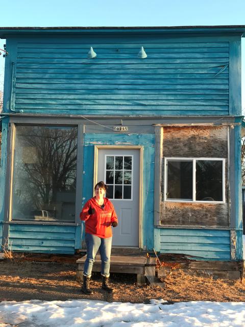 A person stands in front of a weathered blue storefront building during renovation work.